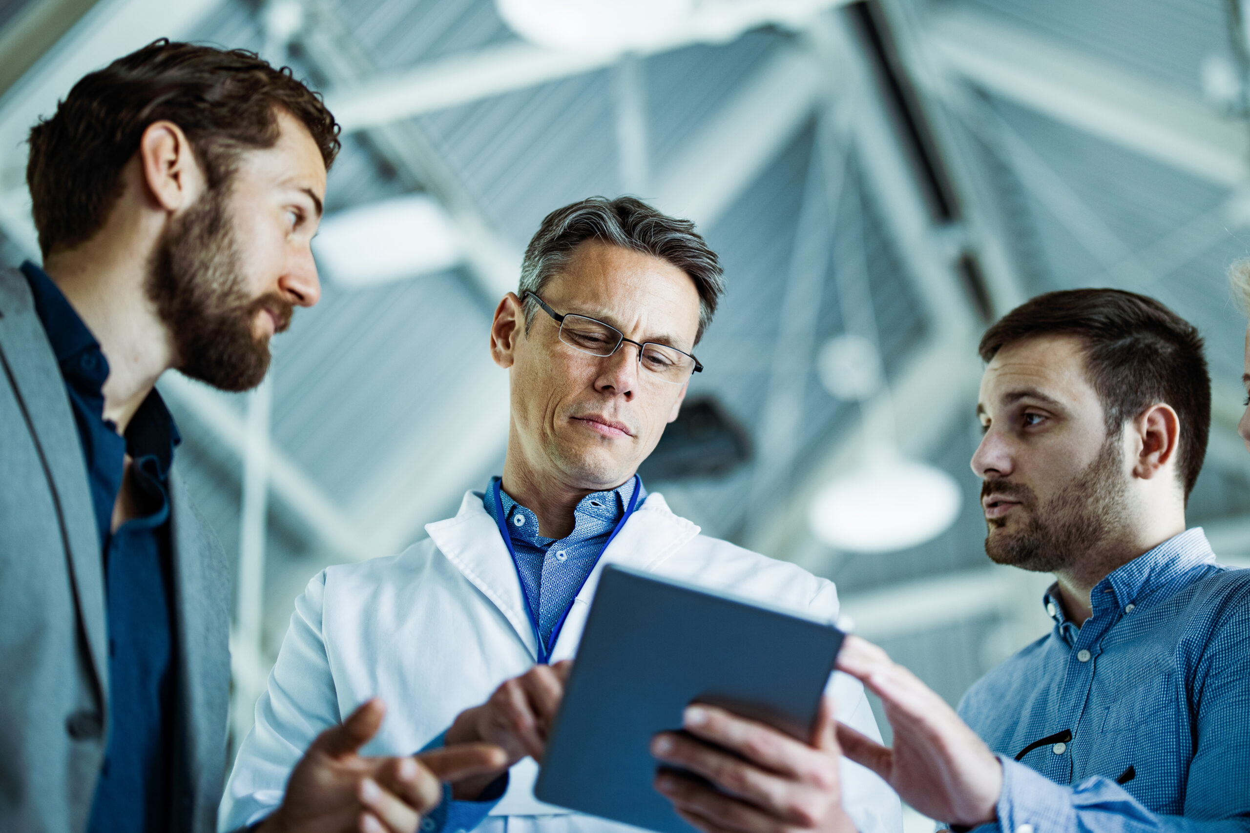 Below view of businessmen and doctor working on touchpad in a hospital. A physician gets updates from his marketing team regarding a recent campaign.